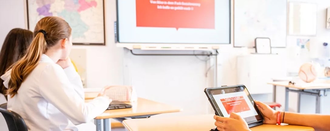 Students in classroom with tablet or iPad and whiteboard in the background