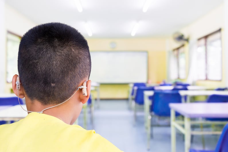 boy with hearing aids sitting at the back of an empty classroom