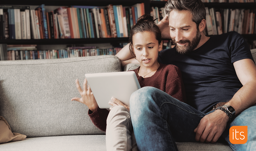 Photo of a father and daughter sitting in their living room while doing school work on a tablet.