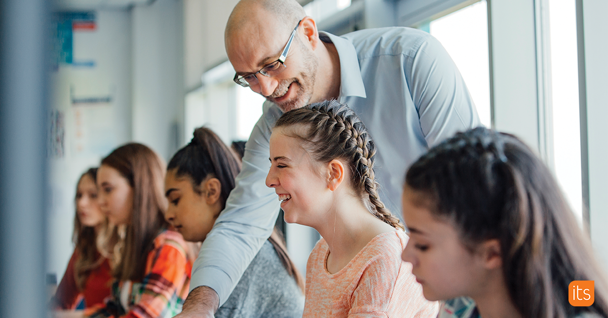 Photo of a group of students sitting in a classroom while being guided by a teacher.