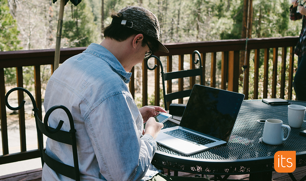 Man sitting in front of a computer while looking down on his phone and bending his neck, demonstrating a classic tech neck.